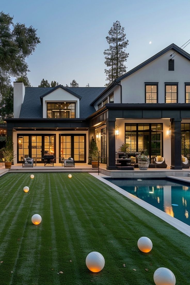 Modern house with large windows, a well-manicured lawn, and a swimming pool at dusk. Turf And Pool Backyard Ideas, Large Grass Backyard Ideas, Small Luxury Backyard Ideas, Turf Grass Backyard Ideas, Turf And Pavers Backyard Pool, Fake Grass Backyard Ideas, Turf In Backyard, White House Backyard, Turf Landscaping Ideas