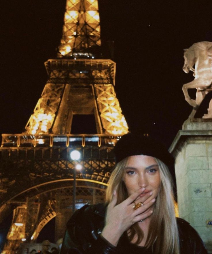 a woman standing in front of the eiffel tower at night with her hand on her mouth