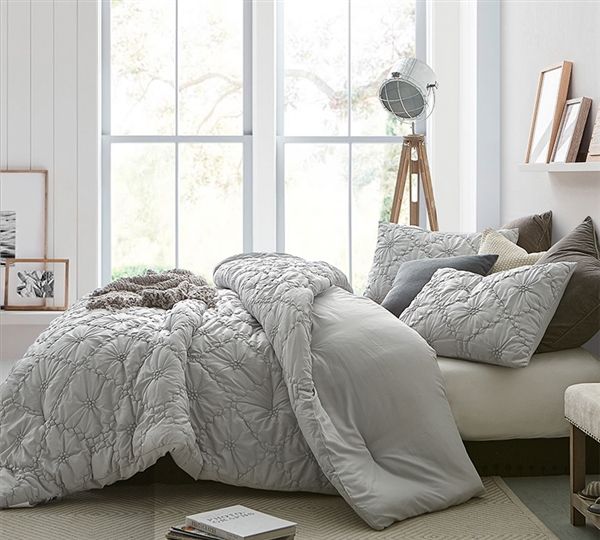 a bedroom with white walls and flooring has a large bed covered in grey comforter