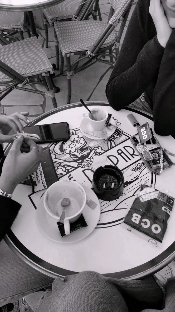 two people sitting at a table with coffee and cell phones