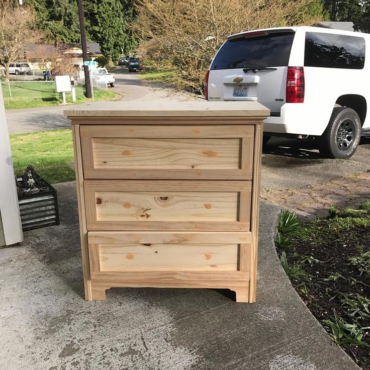 a white van parked next to a wooden dresser on the side of a road in front of a house