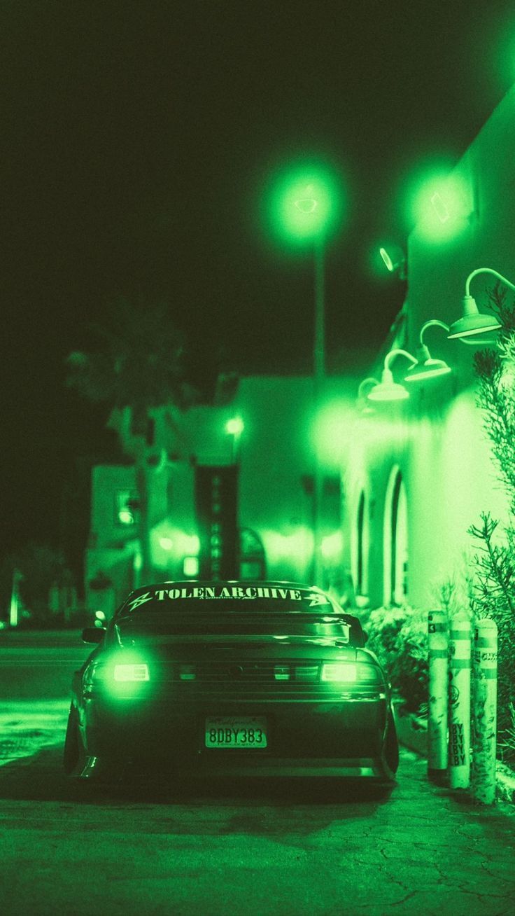 a car parked in front of a building on a street at night with green lights