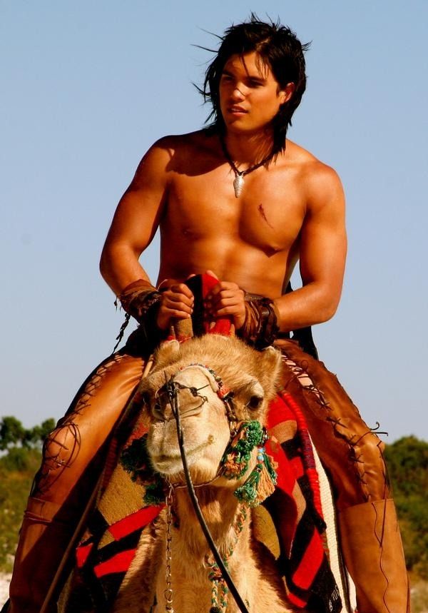 a shirtless man riding on the back of a camel while wearing jewelry and headdress