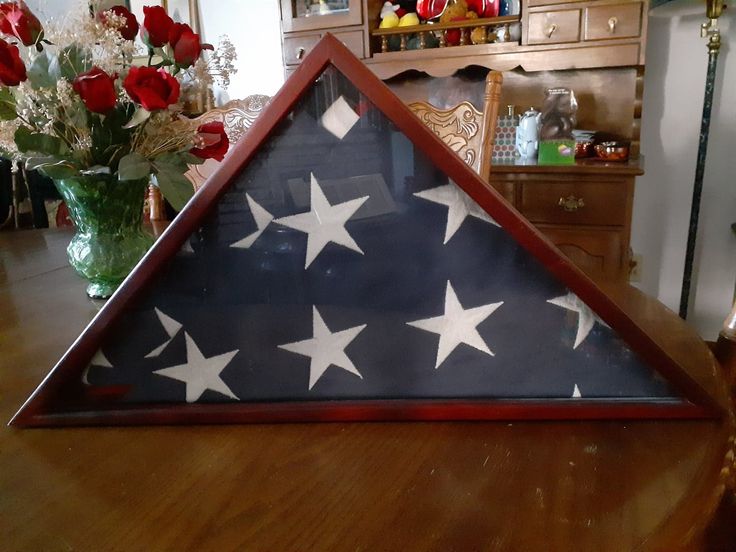 a wooden table topped with a vase filled with flowers and a flag shaped shadow box