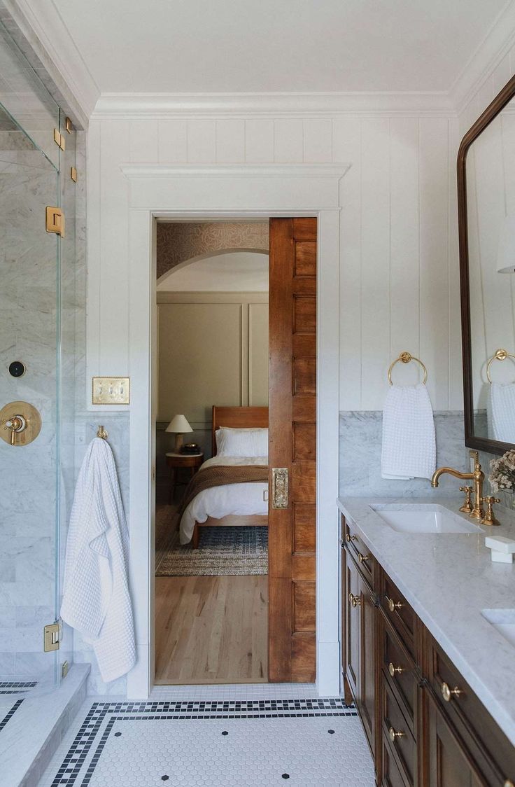 a bathroom with marble counter tops and wooden door leading to a bed in the background