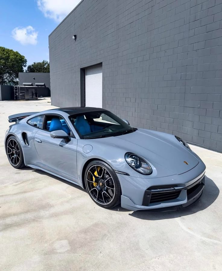 a grey porsche sports car parked in front of a gray building with black rims