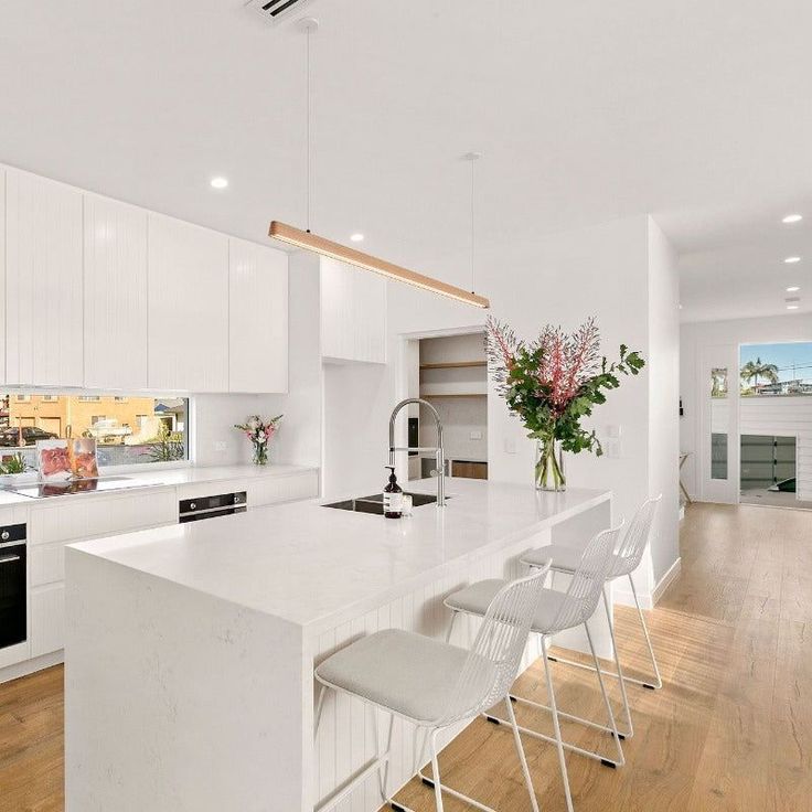 a large kitchen with white cabinets and counter tops, along with bar stools that match the hardwood flooring