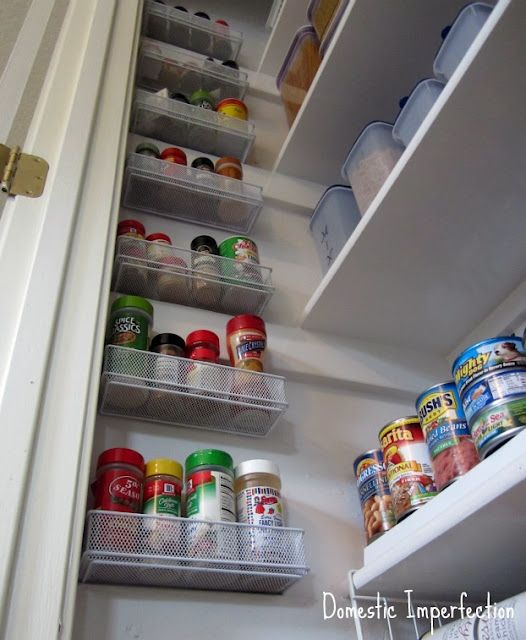 an open refrigerator door with canned food in the bottom shelf and labeled pantry storage below