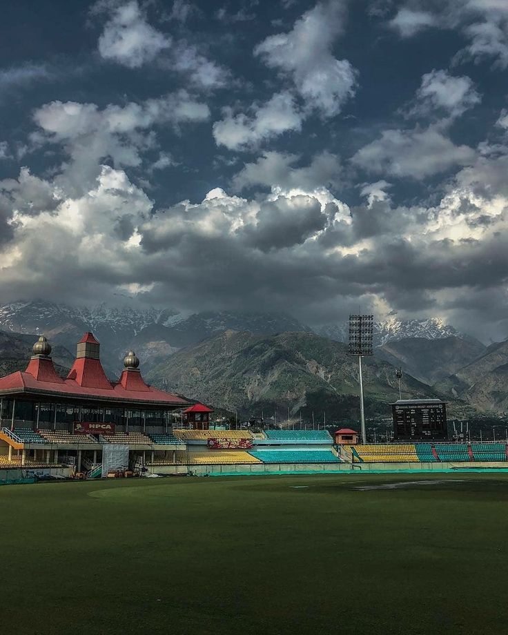 a baseball field with mountains in the background and cloudy skies above it on a sunny day