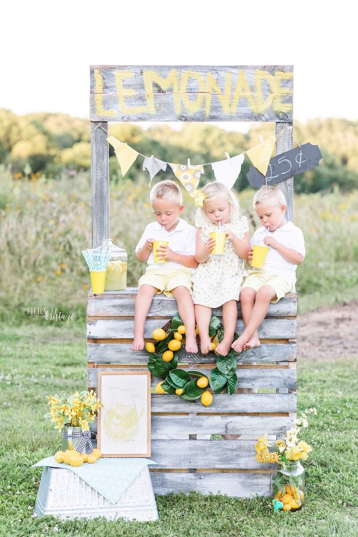 three young children sitting on top of a wooden crate with lemonade in front of them