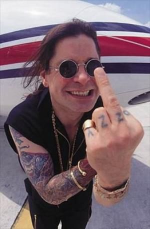 a man with tattoos giving the peace sign in front of an airplane