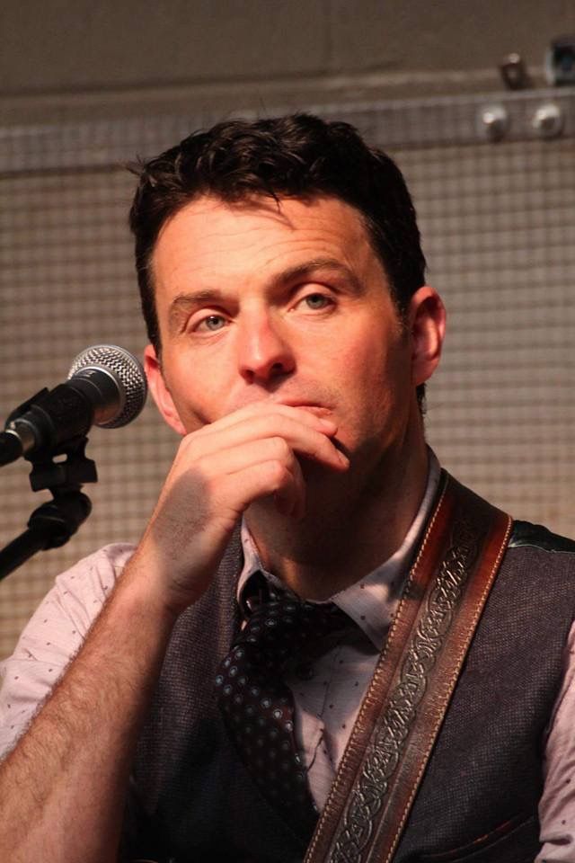 a man in vest and tie holding his hand to his mouth while standing next to a microphone