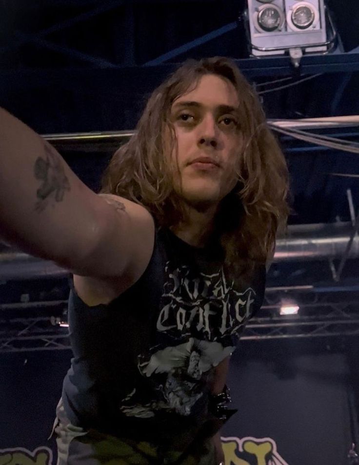 a man with long hair standing in front of a microphone and holding his arm up