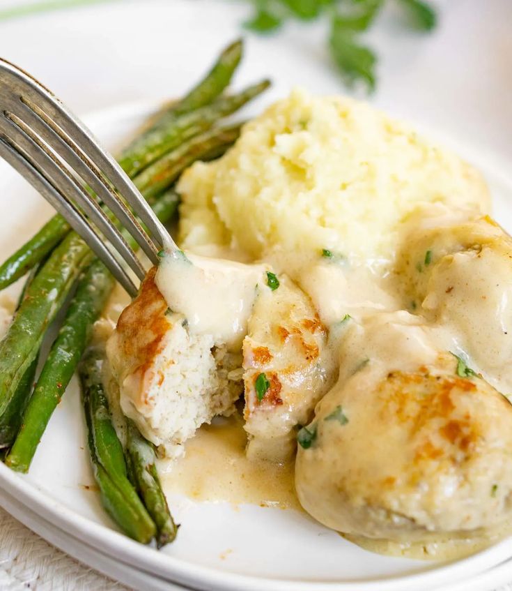 a white plate topped with meatballs covered in gravy and green asparagus