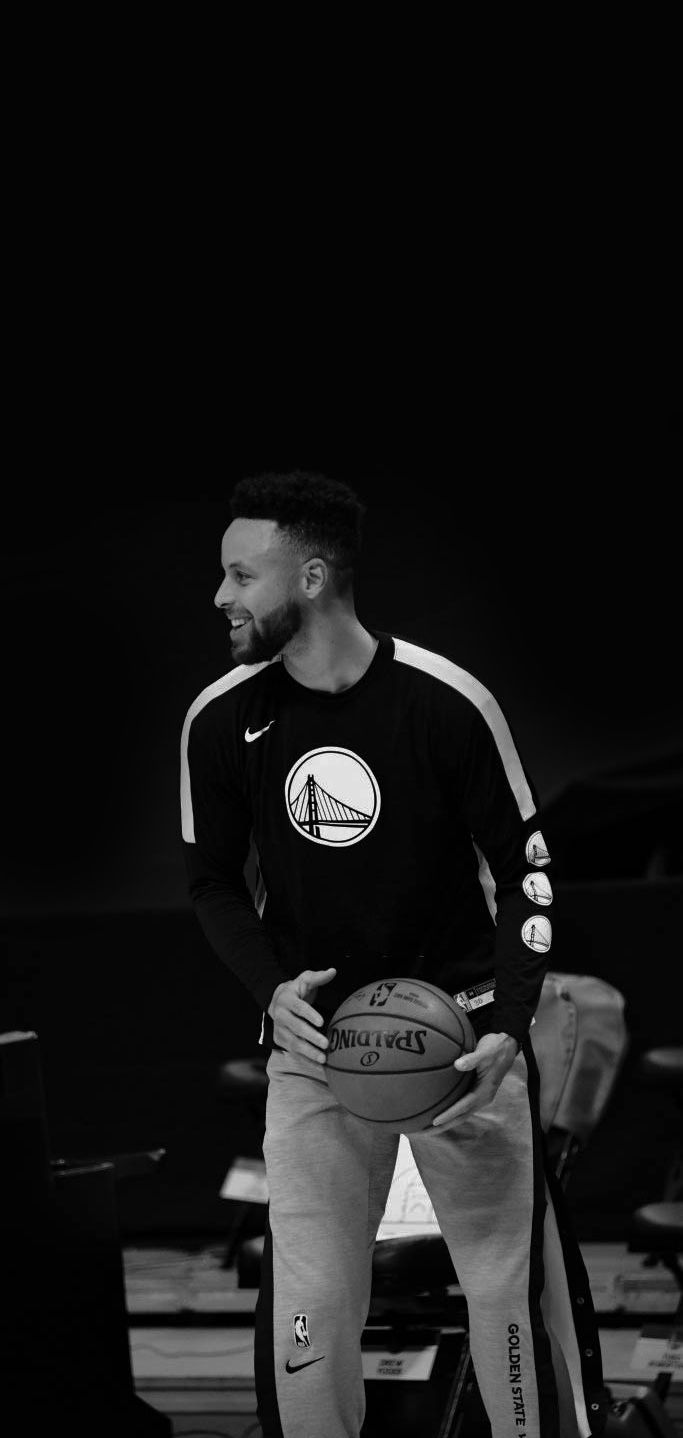 a man holding a basketball while standing in front of a black and white photo with other people