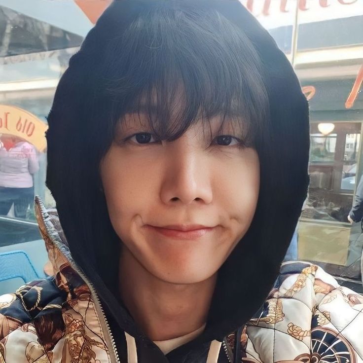 a young man wearing a hoodie and smiling at the camera in front of a store