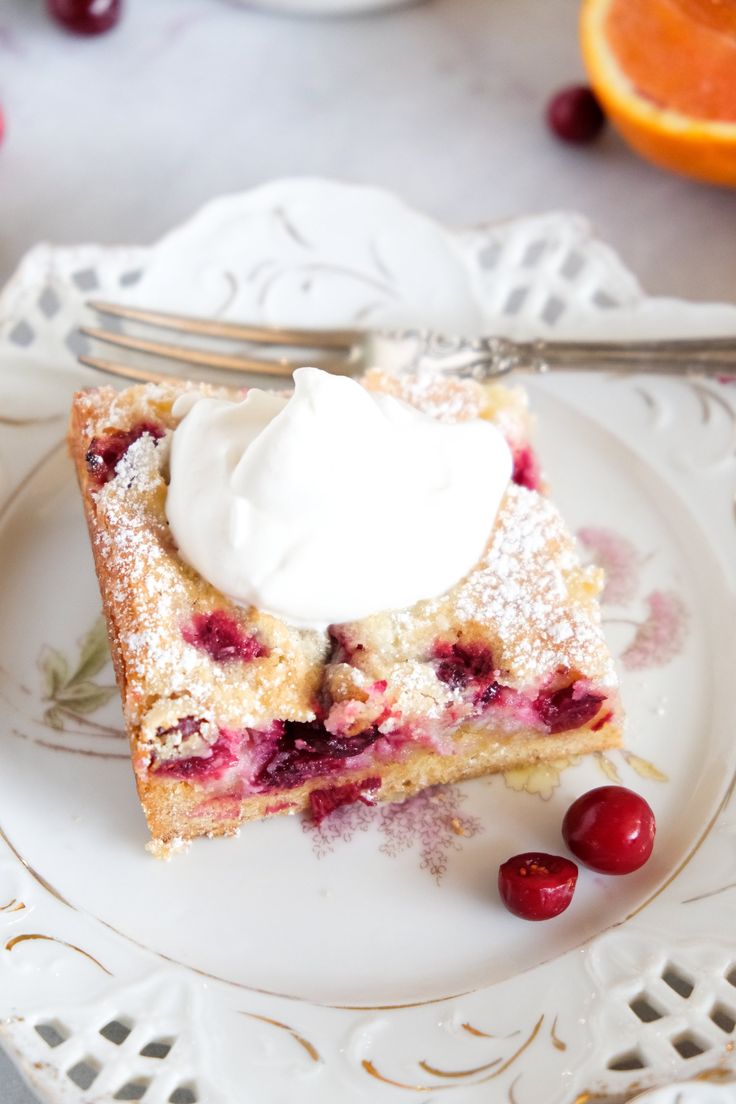 a piece of cake on a plate with whipped cream and cranberries around it