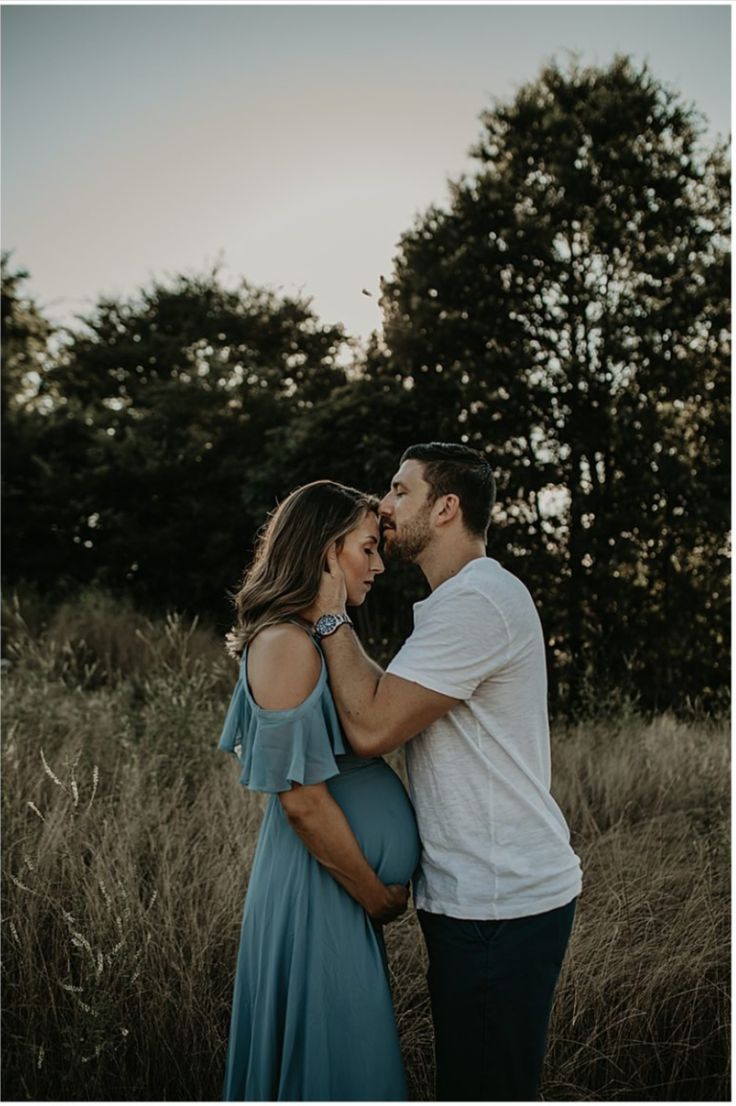 a pregnant couple standing in tall grass at sunset