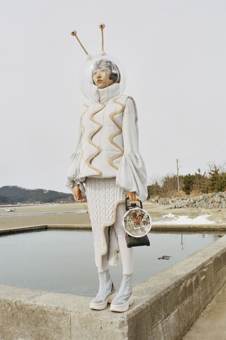 a woman standing on top of a cement wall next to a pond holding a purse