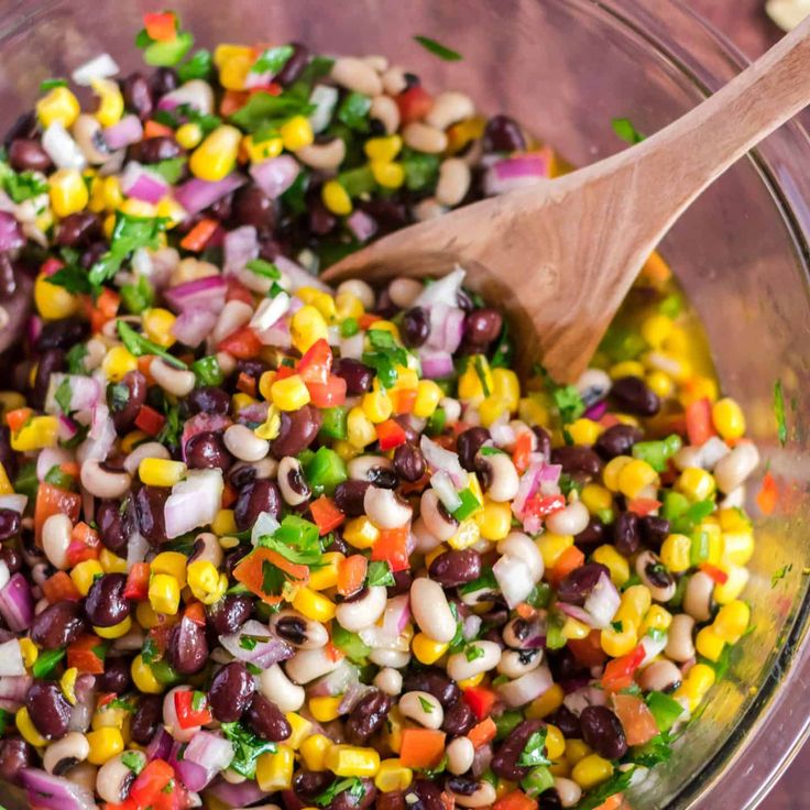 a bowl filled with black beans, corn and cilantro next to a wooden spoon