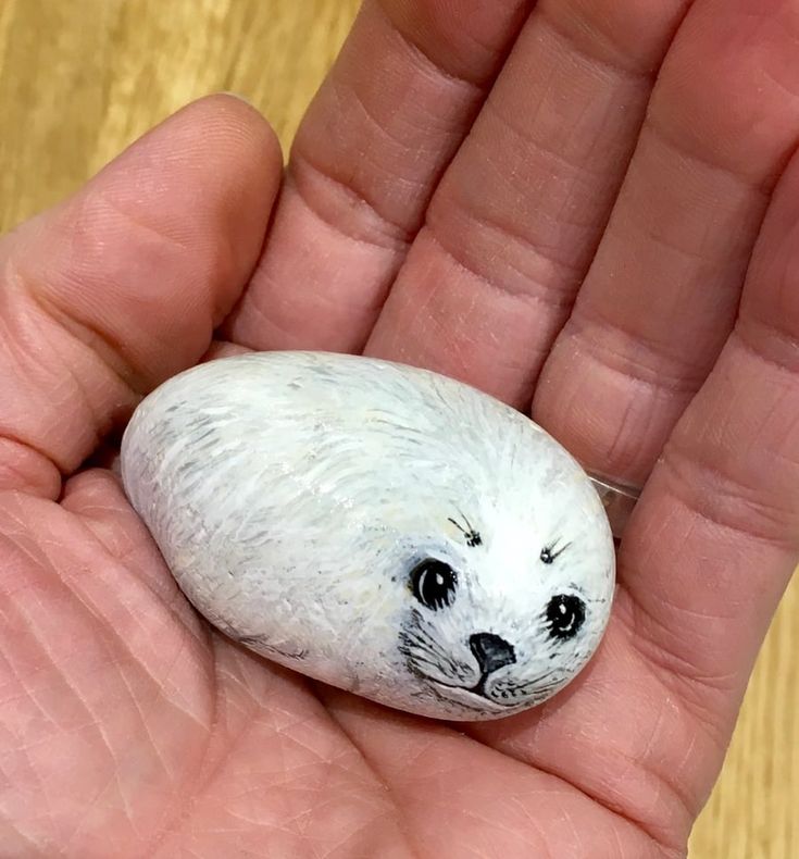 a hand holding a small white rock with a seal on it's face and eyes