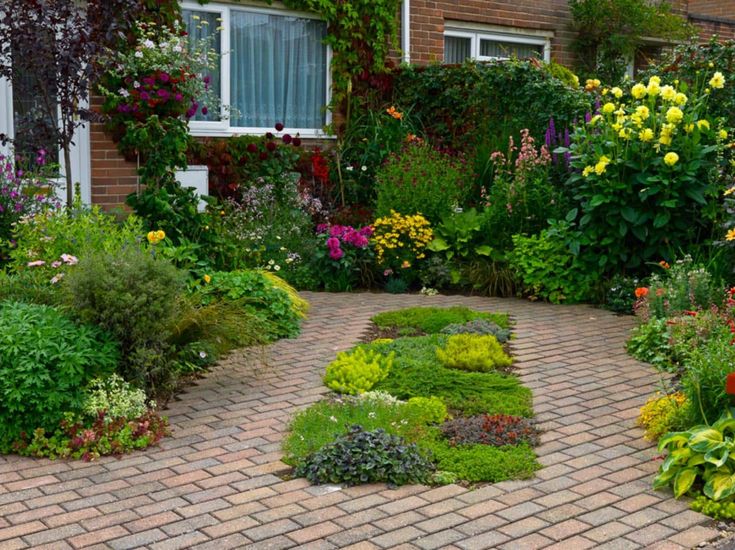 the garden is full of flowers and plants in front of a brick building with white windows