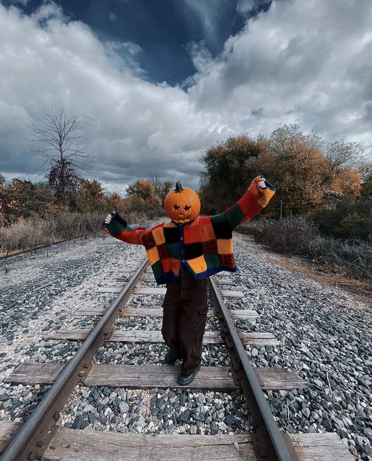 a young child dressed as a pumpkin walking on train tracks with his arms in the air