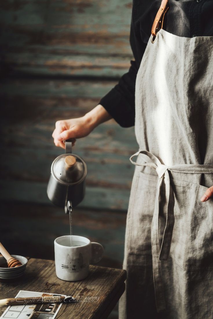 a person in an apron pours coffee into a cup on a wooden table with other items