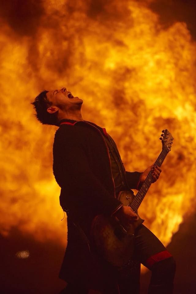 a man playing an electric guitar in front of a large fire filled sky at night