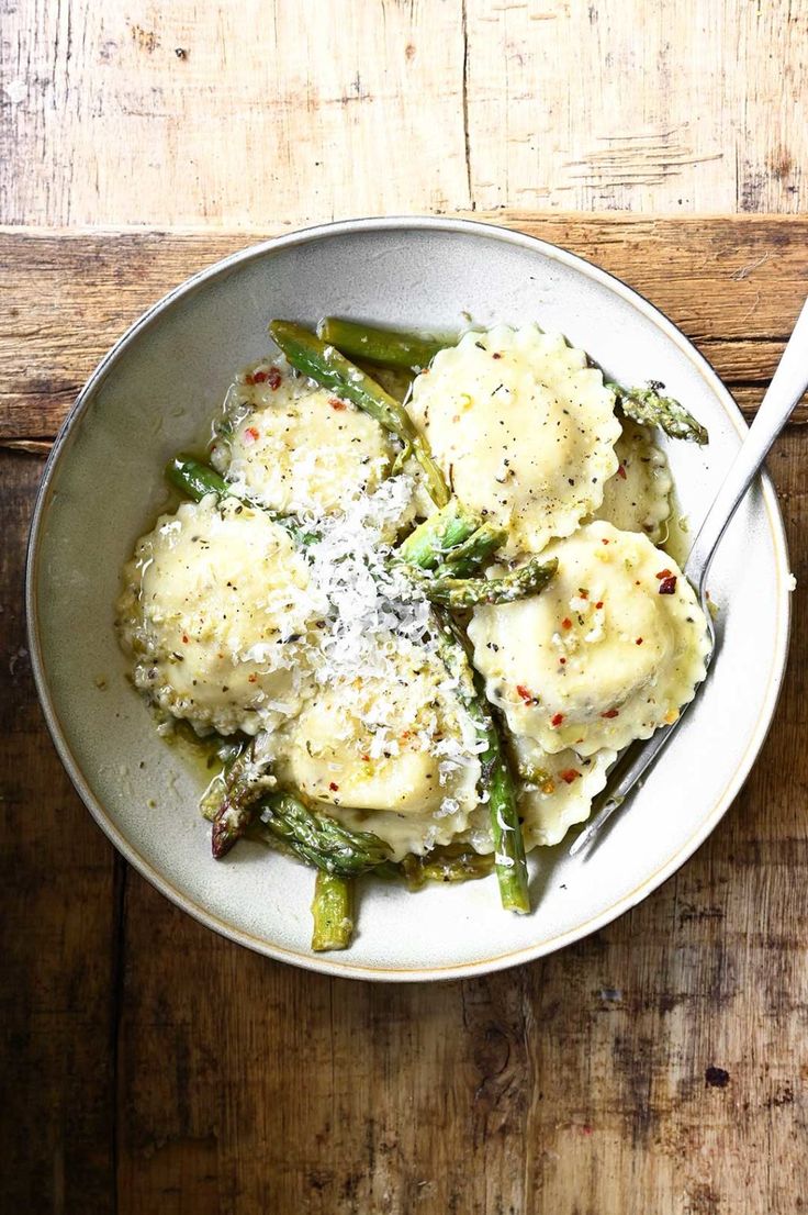 a bowl filled with ravioli and asparagus on top of a wooden table