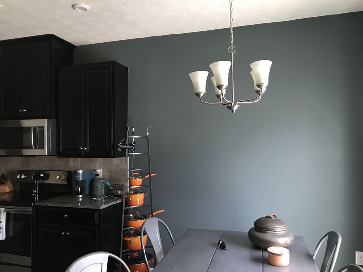 a dining room table and chairs in front of a kitchen with black cabinets, an oven and microwave