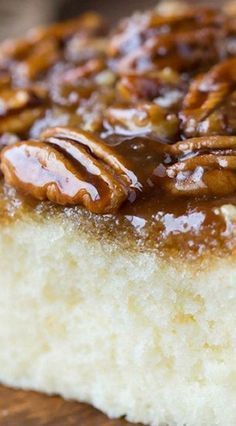 a close up of a piece of cake with pecans on top and caramel sauce