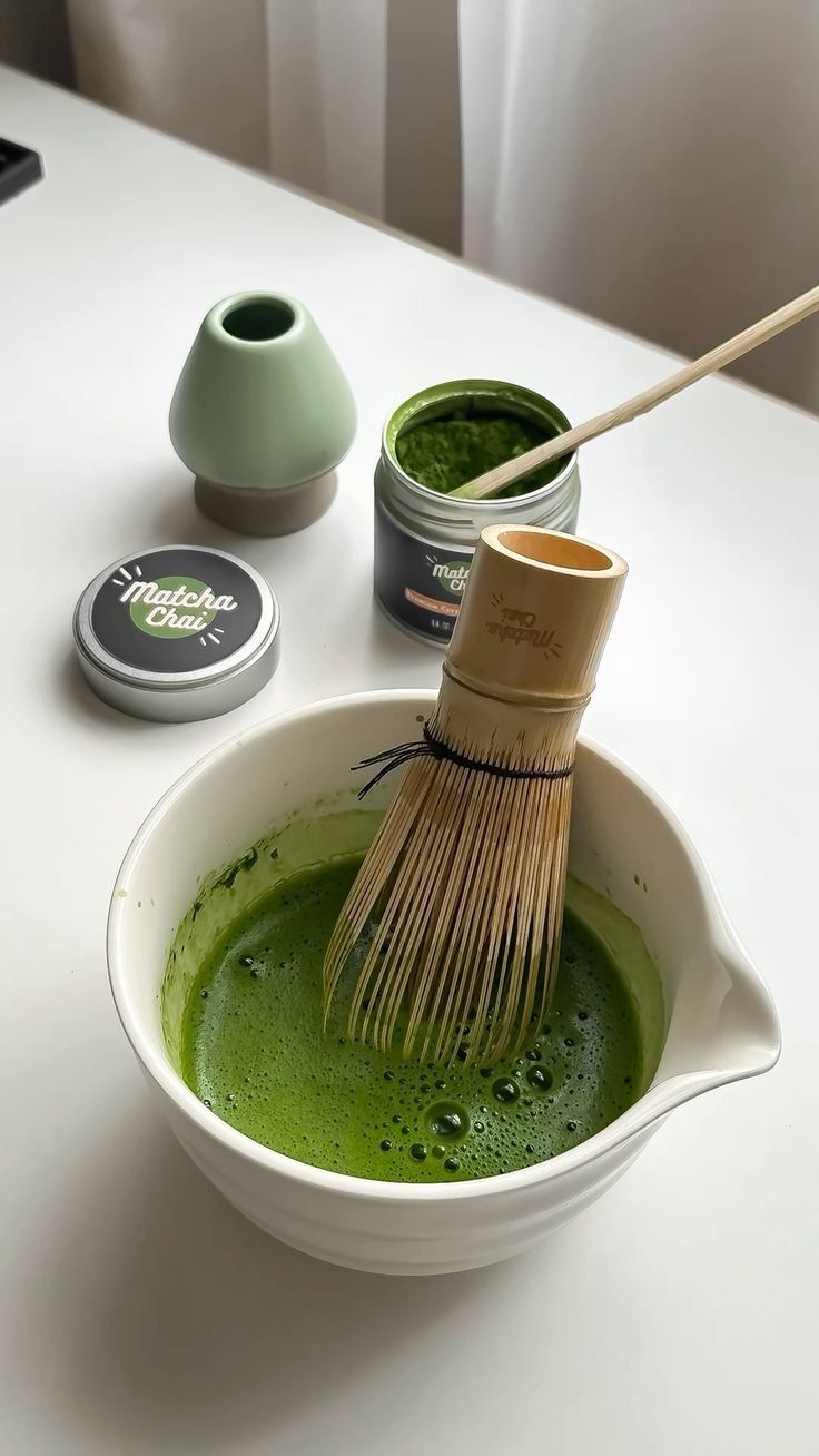 a white bowl filled with green liquid and a wooden whisk