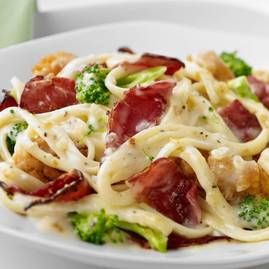 a white plate topped with pasta and broccoli covered in cheese sauce on top of a table