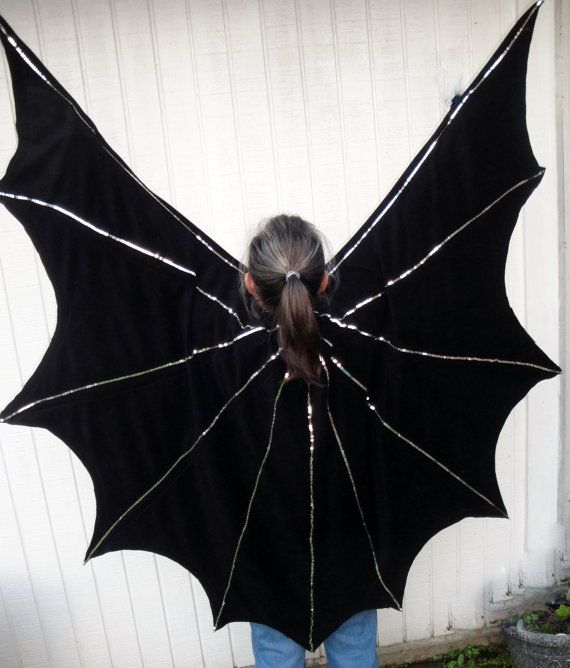 a woman wearing a black bat costume standing in front of a garage door with her back turned to the camera