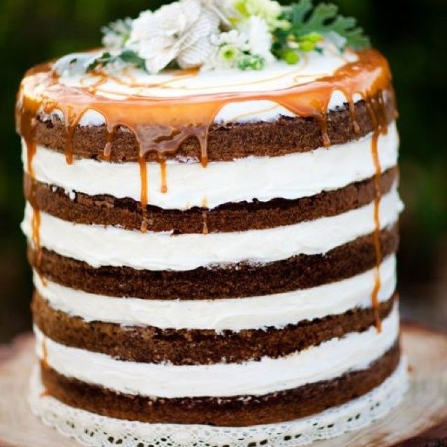 a cake that is sitting on top of a wooden slice with icing and flowers