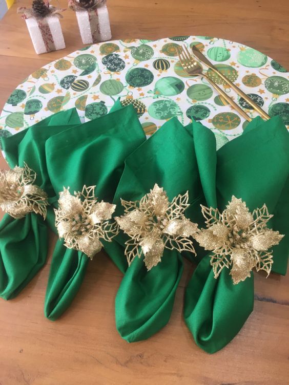 green napkins with gold flowers are sitting on a wooden table next to silverware