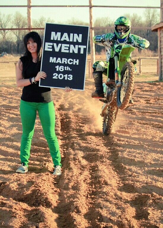 a woman standing next to a dirt bike holding a sign that says main event march 16th 2013