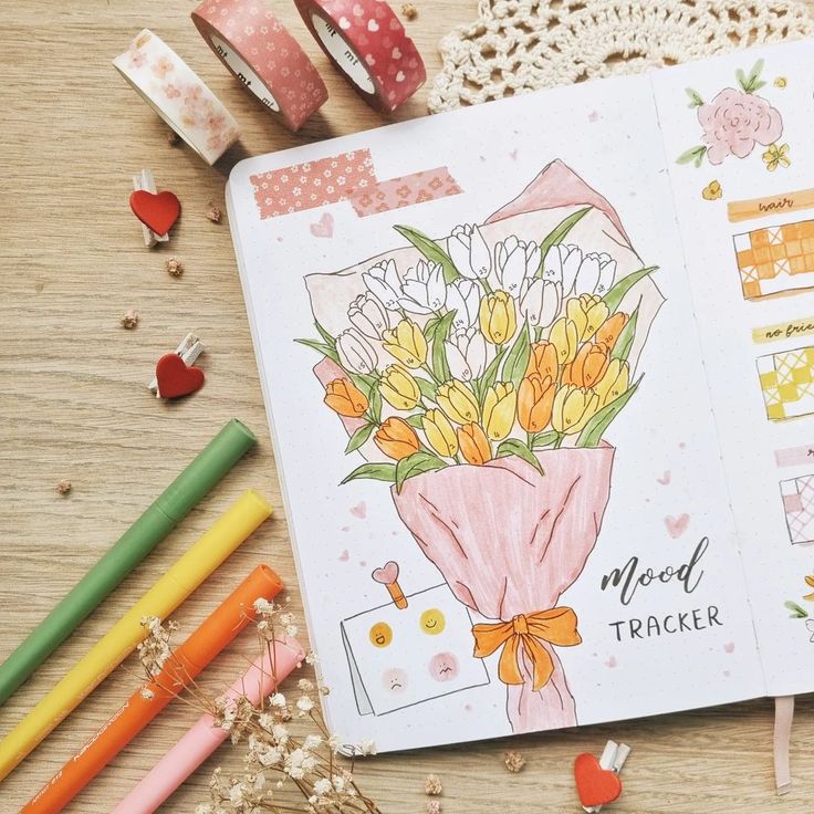 an open notebook with flowers on it next to markers and pencils