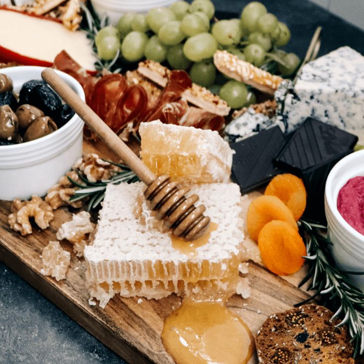 a wooden tray topped with cheeses, crackers and fruit next to other foods