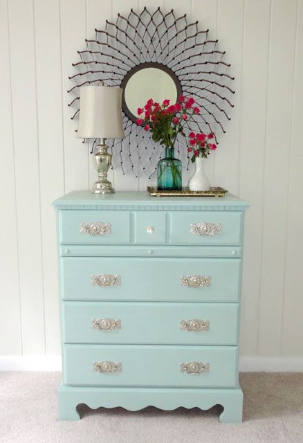 a blue dresser with flowers on top and a mirror above it in a room that has white walls