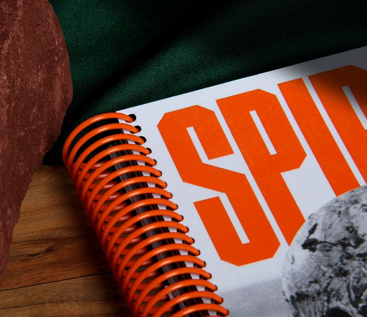 an orange spiral notebook sitting on top of a wooden table next to a red rock