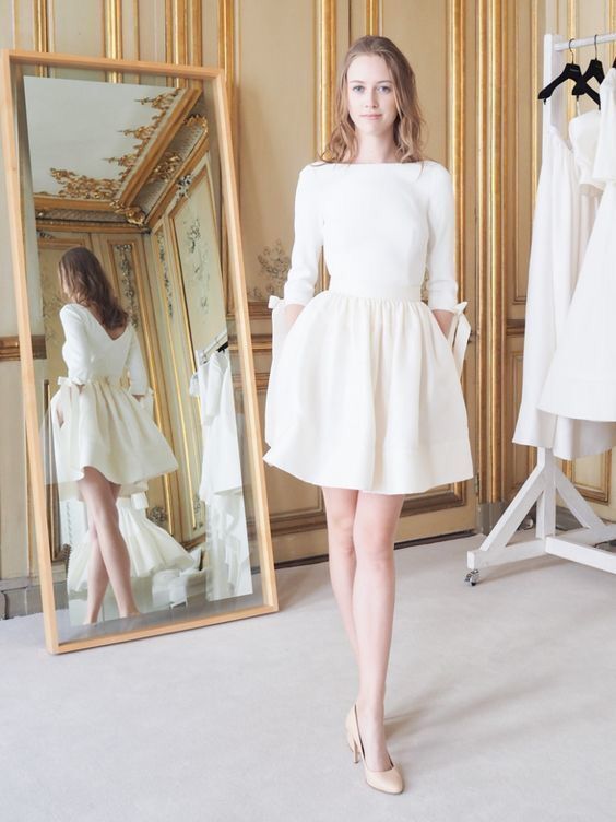 a woman standing in front of a mirror wearing a white dress and high heel shoes