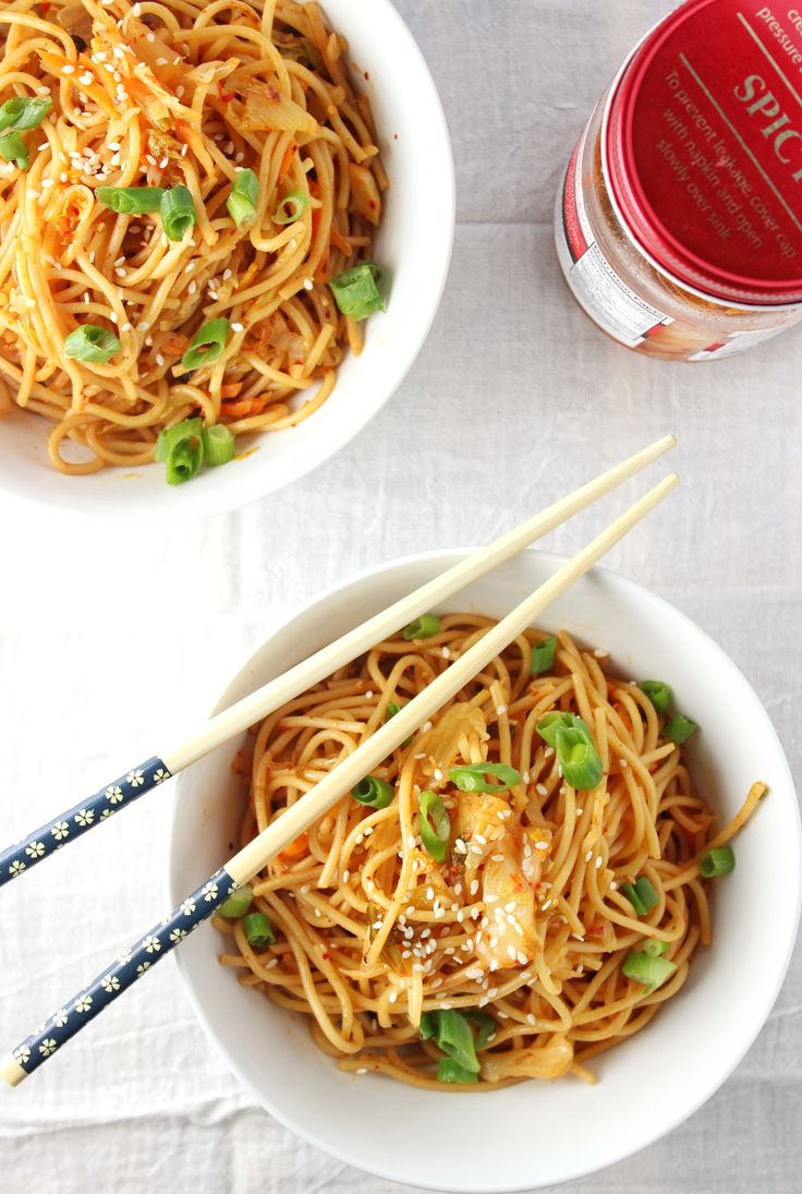 two bowls filled with noodles and chopsticks on top of a white table cloth