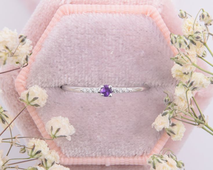 a purple stone ring sitting on top of a pink velvet covered pillow next to white flowers