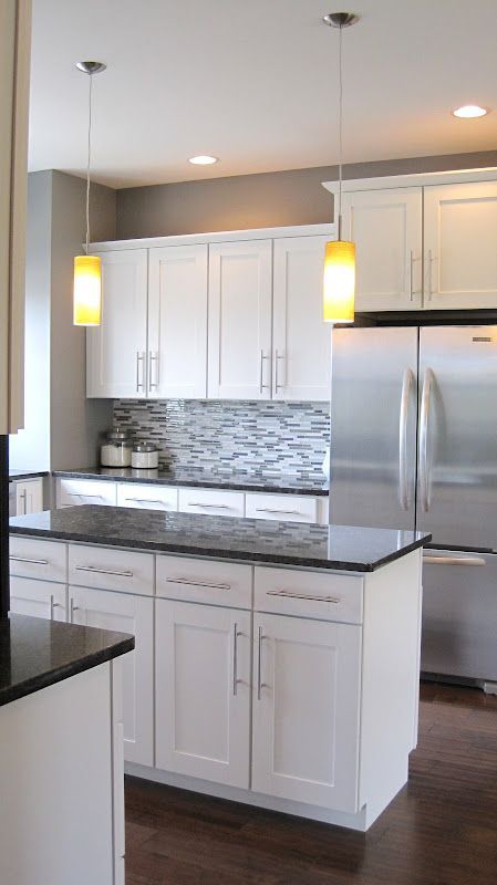 a kitchen with white cabinets and black counter tops, along with a stainless steel refrigerator