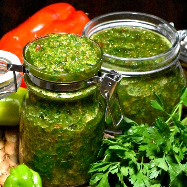 two jars filled with pesto next to vegetables