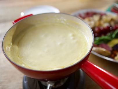 a red sauce pot sitting on top of a stove next to a plate of food