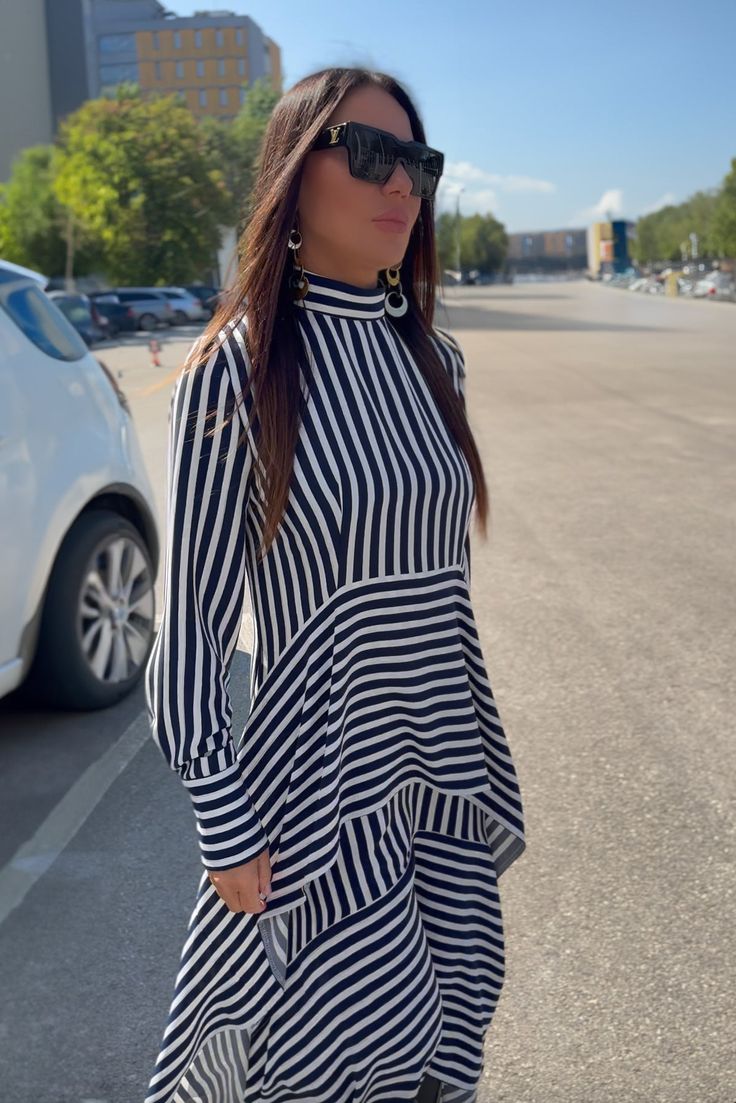 This stunning blue and white striped dress is made from polyviscose, featuring a half-turtleneck and a zip closure at the back. The dress has two asymmetrical ruffles and long sleeves with buttoned cuffs. Its unique and modern design is suitable for various body types, offering a loose fit that doesn't cling to the body, providing comfort and freedom of movement. The asymmetry and elegant style make this dress a fashionable choice for any occasion. Made of: Viscous Polyester This top can be cust Long Sleeve Dresses With Vertical Stripes For Work, Long Sleeve Vertical Stripes Work Dress, Long Sleeve Vertical Stripe Work Dresses, Striped Long Sleeve Midi Dress For Work, Chic Striped Mini Dress With Ruffles, Chic Striped Long Sleeve Midi Dress, Elegant Striped Long Sleeve Mini Dress, Elegant Striped Long Sleeve Midi Dress, Chic Long Sleeve Dresses With Vertical Stripes