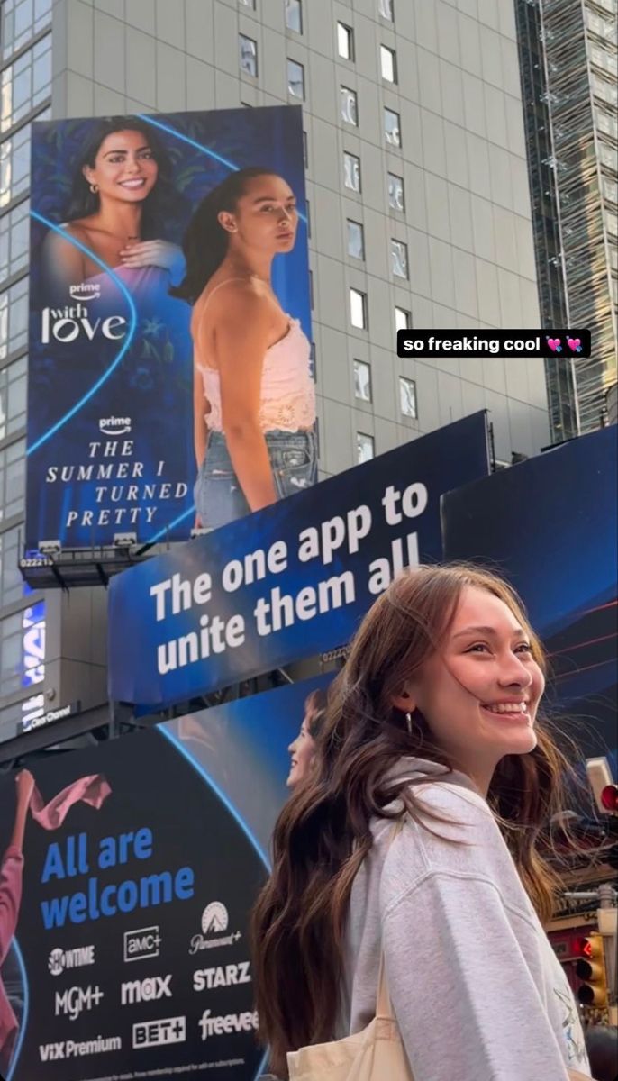 a woman walking down the street in front of tall buildings with billboards on it